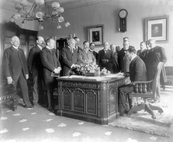 Secretary of State John Hay signs a peace treaty with Spain at the Resolute desk